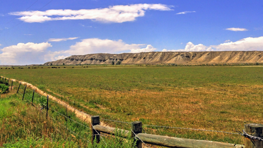 Open grassland with fence line and mesa backdrop under blue sky in southern Colorado.