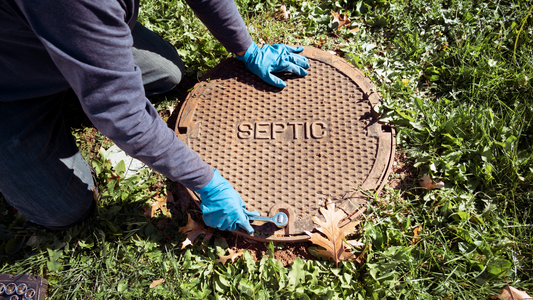 Technician opening a septic tank access lid to inspect the system before service.