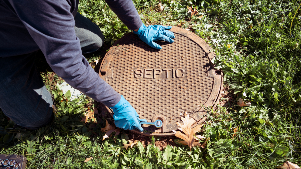 Technician opening a septic tank access lid to inspect the system before service.